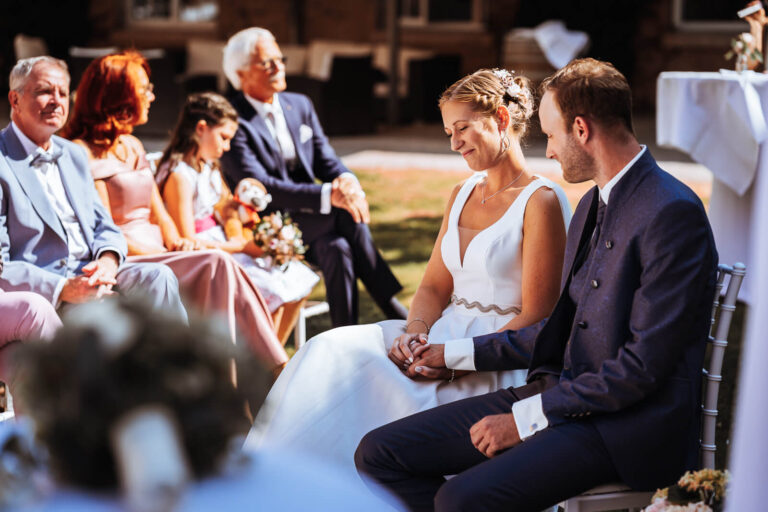 Brautpaar h&auml;lt sich die H&auml;nde und genie&szlig;t den Moment am Schloss W&ouml;ltingerode, G&auml;ste im Hintergrund, nat&uuml;rlicher Hochzeitsmoment