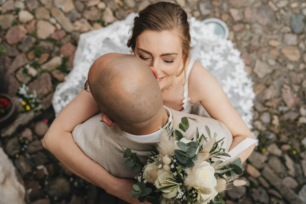 Vogelperspektive bei der Edelkastanie Voitze: Braut umarmt ihren Ehemann und l&auml;chelt, Hochzeitsmoment nahe der Location
