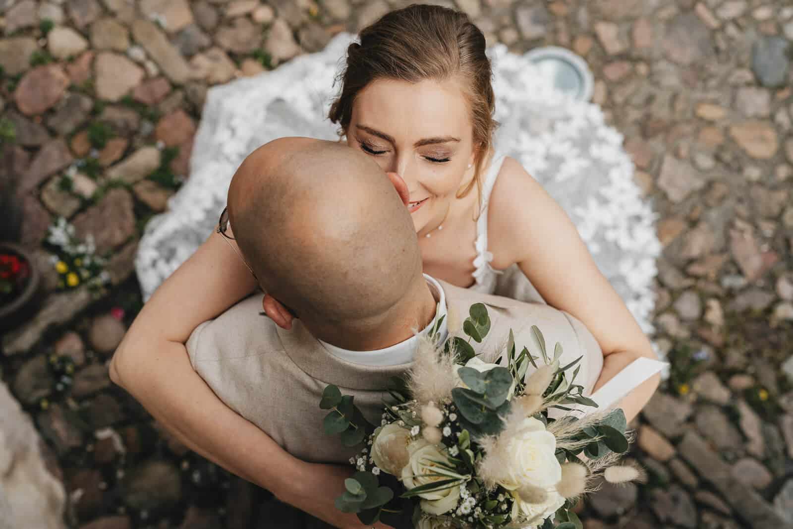 Vogelperspektive bei der Edelkastanie Voitze: Braut umarmt ihren Ehemann und lächelt, Hochzeitsmoment nahe der Location