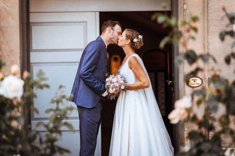 Brautpaar k&uuml;sst sich vor einer T&uuml;r am Schloss W&ouml;ltingerode und h&auml;lt gemeinsam den Blumenstrau&szlig;, romantischer Hochzeitsmoment