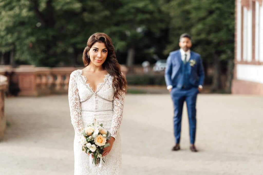 Brautpaarshooting am Schloss Philippsruhe in Hanau: Braut ist scharf im Vordergrund, Br&auml;utigam steht unscharf im Hintergrund, romantischer Moment