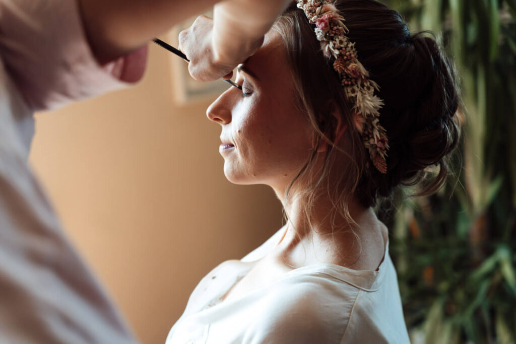 Frau wird beim Getting Ready am Fenster im Zimmer geschminkt, fotografiert vom Hochzeitsfotograf Wolfsburg