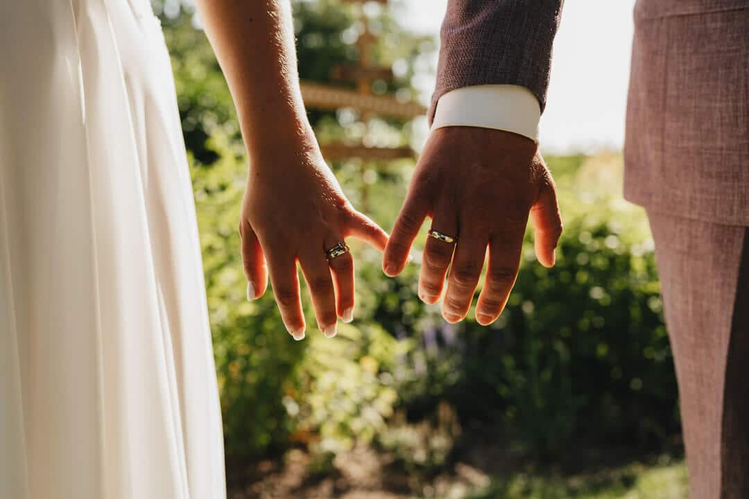 Nahaufnahme der Ringe bei Sonnenuntergang im Garten in Adensbüttel: Zeigefinger des Brautpaars berühren sich, Detailfoto