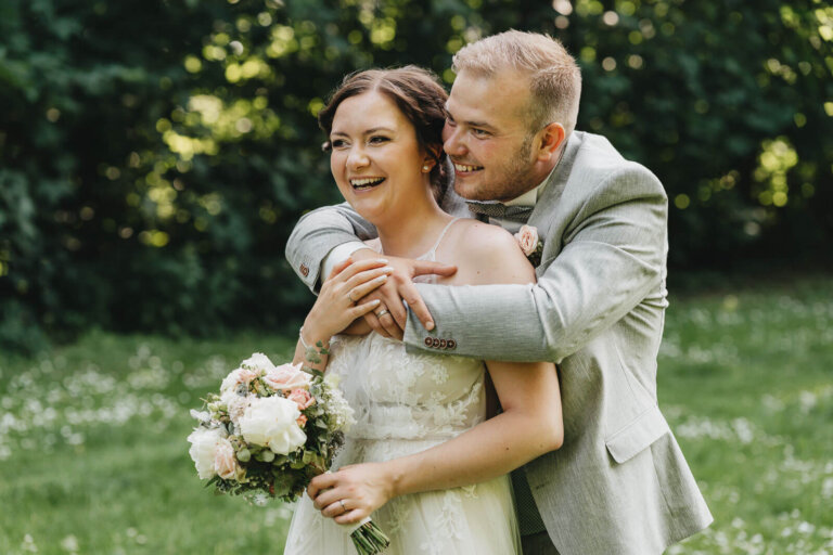 Brautpaarshooting in Heese 5: Braut hält den Strauß, Brautpaar lächelt, Bräutigam umarmt die Braut, natürlicher Moment