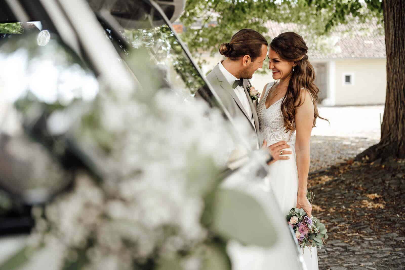 Brautpaarshooting am Schloss Destedt: VW Bulli im Vordergrund unscharf, Bräutigam fasst die Braut an der Hüfte, romantischer Moment