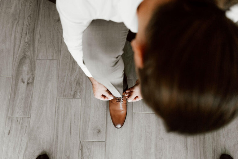 Vogelperspektive beim Getting Ready zuhause: Bräutigam bindet sich den Schuh, natürlicher Vorbereitungsmoment vor der Hochzeit