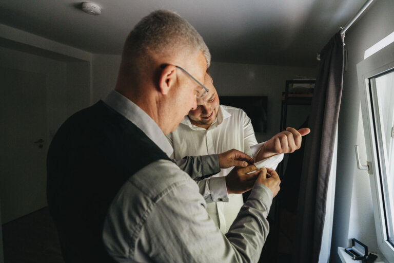 Getting Ready des Bräutigams in Heese 5: Trauzeuge hilft dem Bräutigam, die Manschettenknöpfe anzubringen, Detailmoment vor der Hochzeit