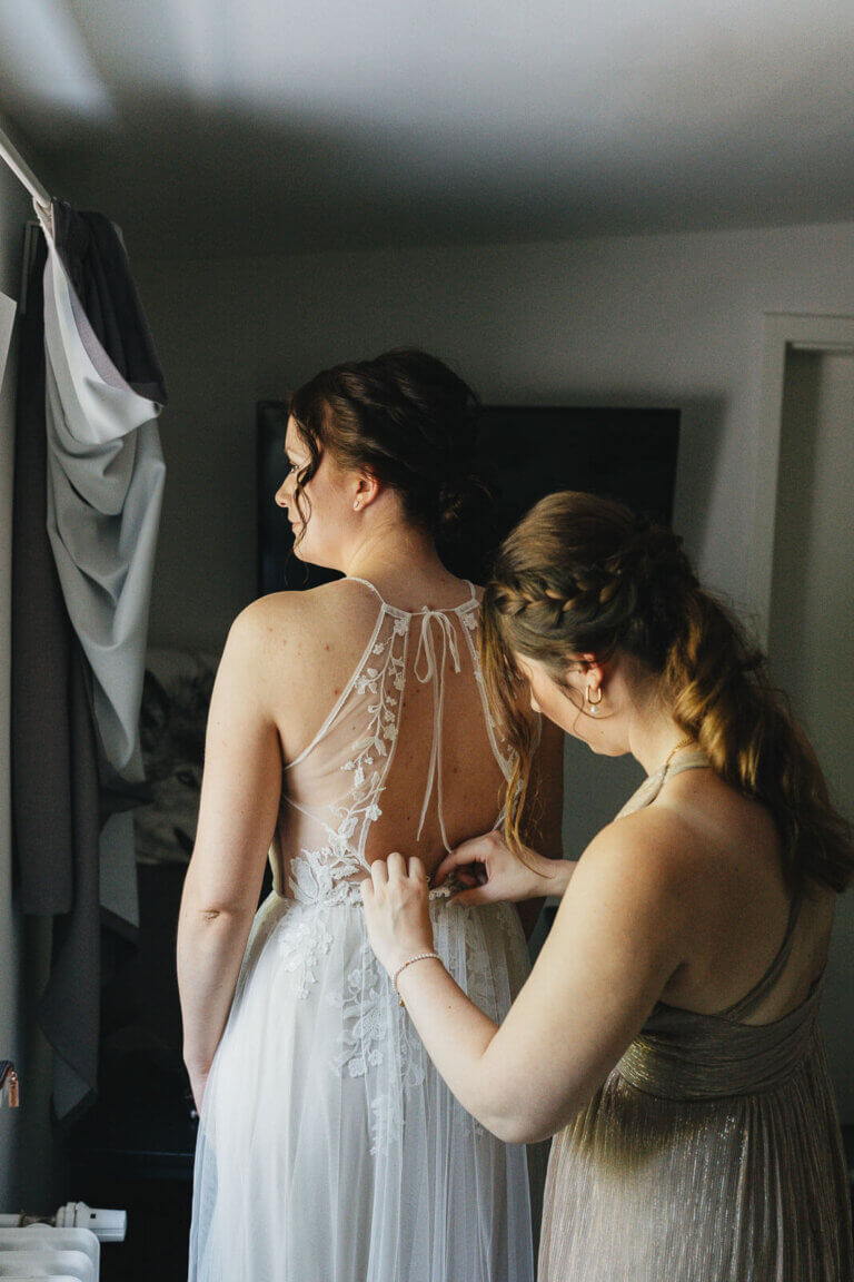 Getting Ready der Braut in Heese 5: Trauzeugin knüpft der Braut das Kleid zu, emotionaler Vorbereitungsmoment