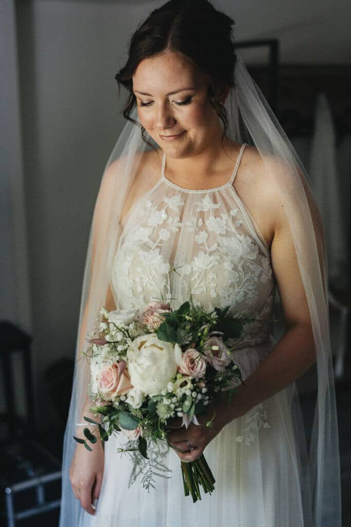 Getting Ready der Braut in Heese 5: Braut steht am Fenster und schaut ihren Brautstrauß an, ruhiger Moment im natürlichen Licht