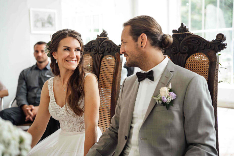 Freie Trauung im Schloss Destedt: Brautpaar sitzt am Altar, schaut sich an und lächelt, emotionaler Moment während der Zeremonie