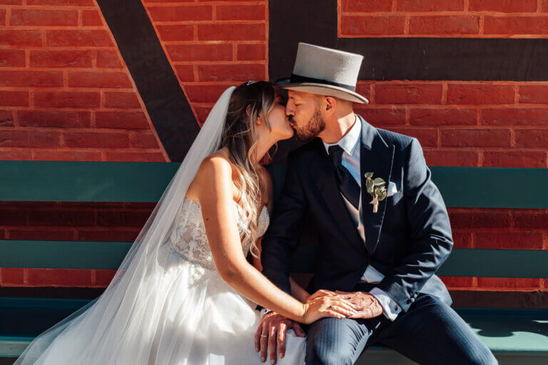 Bräutigam mit Zylinder küsst seine Frau auf einer Bank, romantischer Vintage-Hochzeitsmoment