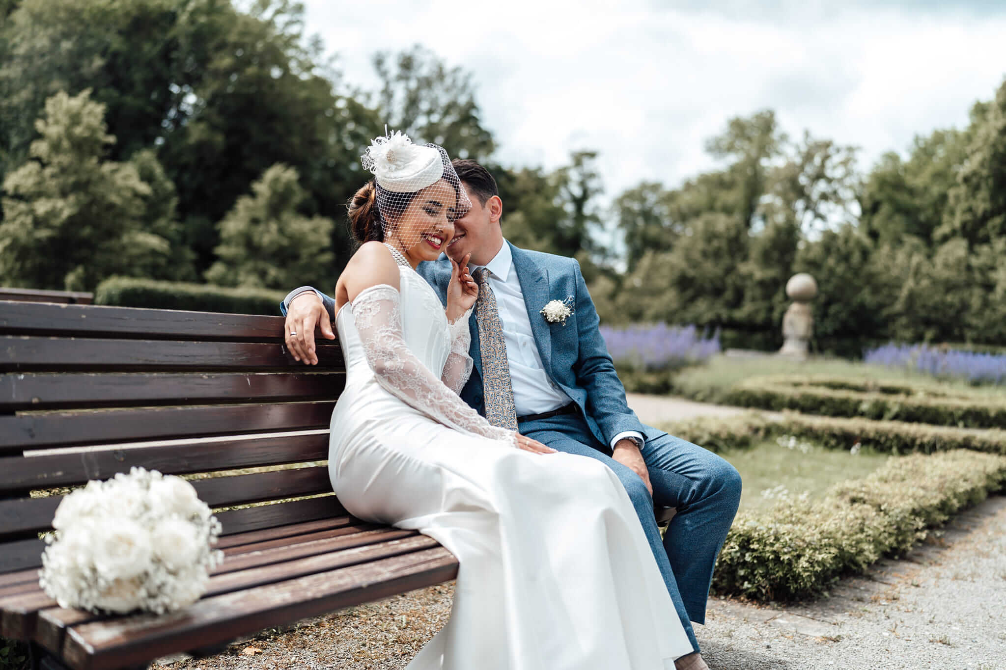 Brautpaar sitzt auf einer Bank, Bräutigam flüstert der Braut etwas ins Ohr, Braut lächelt, intimer Moment
