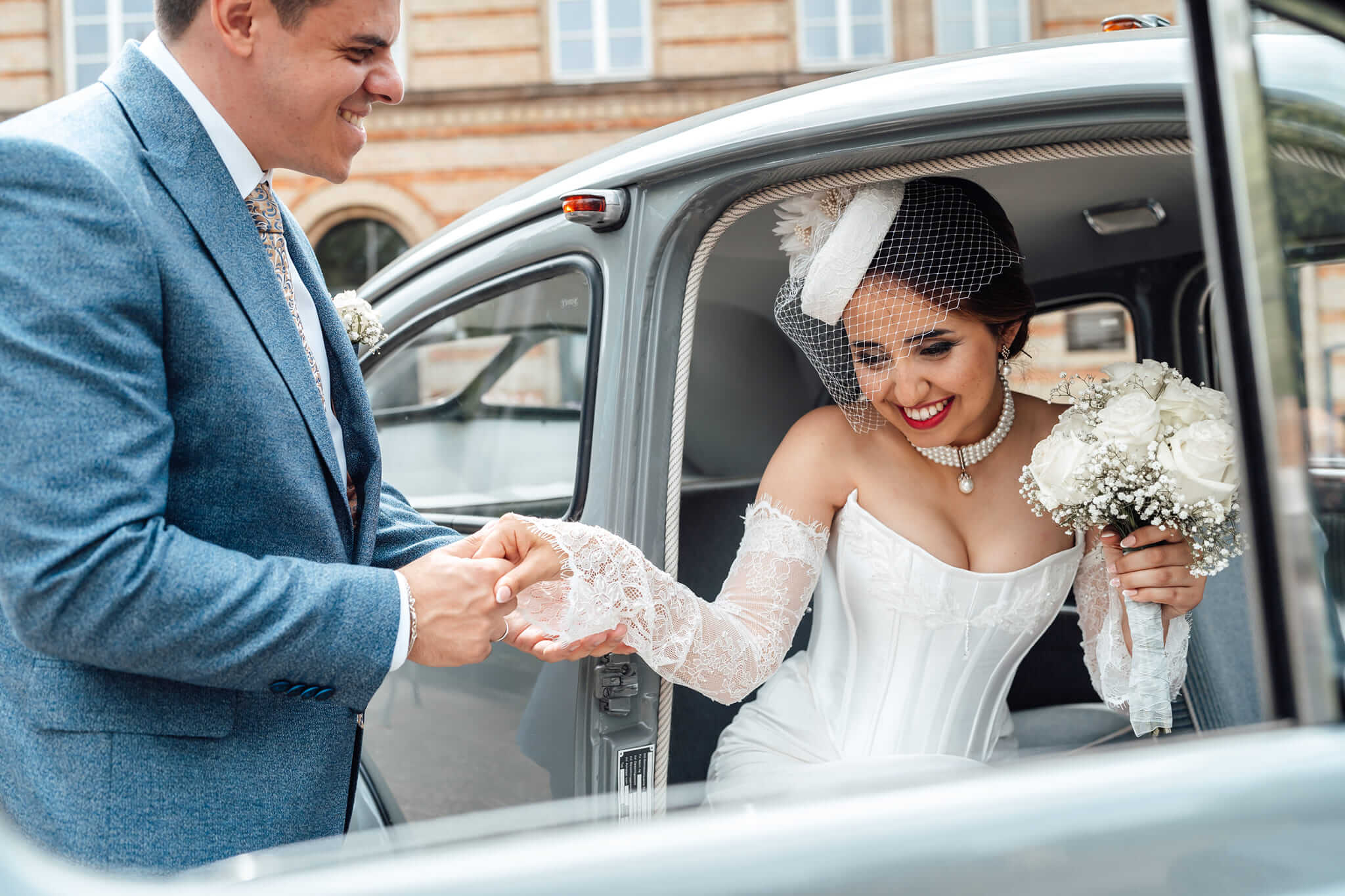 Bräutigam hält die Autotür eines Oldtimer Mercedes auf und hält die Hand seiner Frau, romantischer Hochzeitsmoment