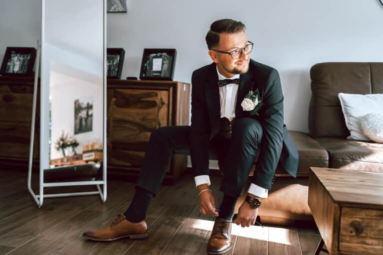 Bräutigam Getting Ready im Harz sitzt auf dem Sofa und bindet seine Schuhe vor der Hochzeit