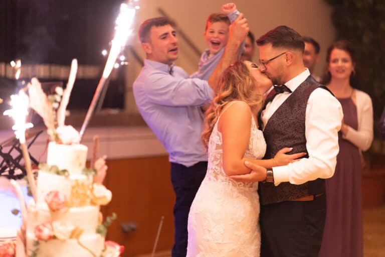 Brautpaar küsst sich beim Hochzeitstortenmoment in Braunschweig während ein Kind im Hintergrund begeistert jubelt