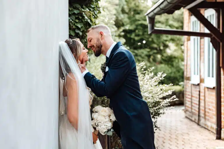 Hochzeitsfotograf Braunschweig – Braut lehnt an einer Wand, während der Bräutigam sie liebevoll am Hals hält und kurz vor einem Kuss steht